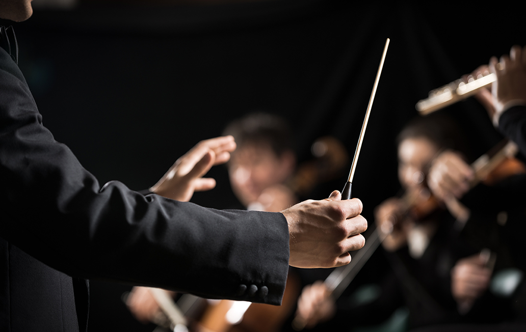 Conductor directing symphony orchestra with performers on background, hands close-up.